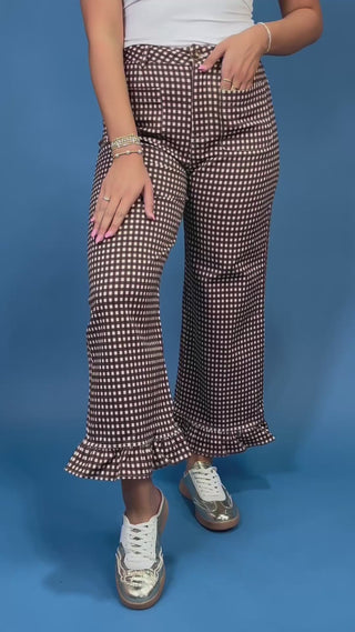 A person wearing high-waisted, wide-leg pants with a brown and white micro-check pattern and ruffled hems, paired with white sneaker