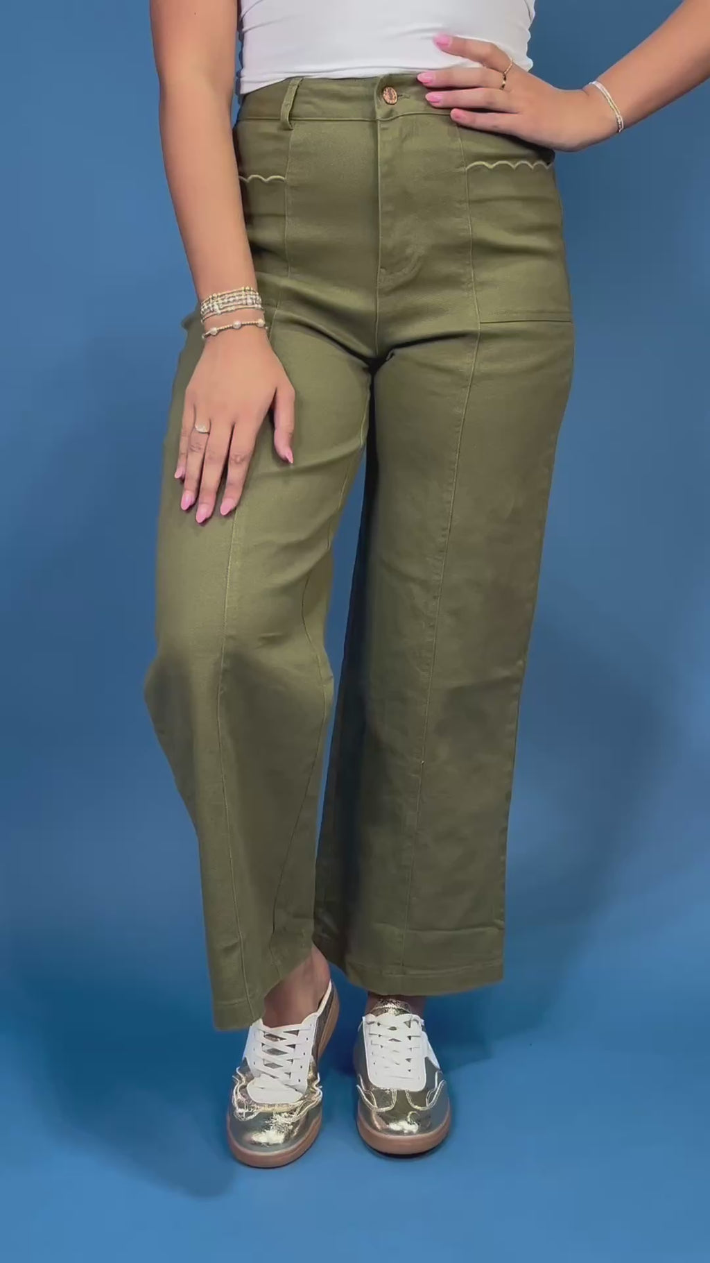 A person wearing olive green wide-leg cropped pants with decorative zigzag stitching on the front pockets, paired with a white top and white sneakers