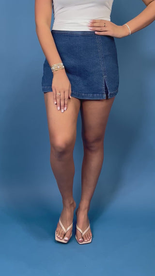 Dark wash denim skort with a flattering fitted silhouette, contrast stitching, and a chic front slit detail.