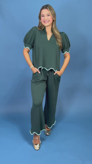 a dark green two-piece outfit consisting of a short-sleeve top with puff sleeves and a scalloped hem, paired with matching wide-leg pants with white piping trim