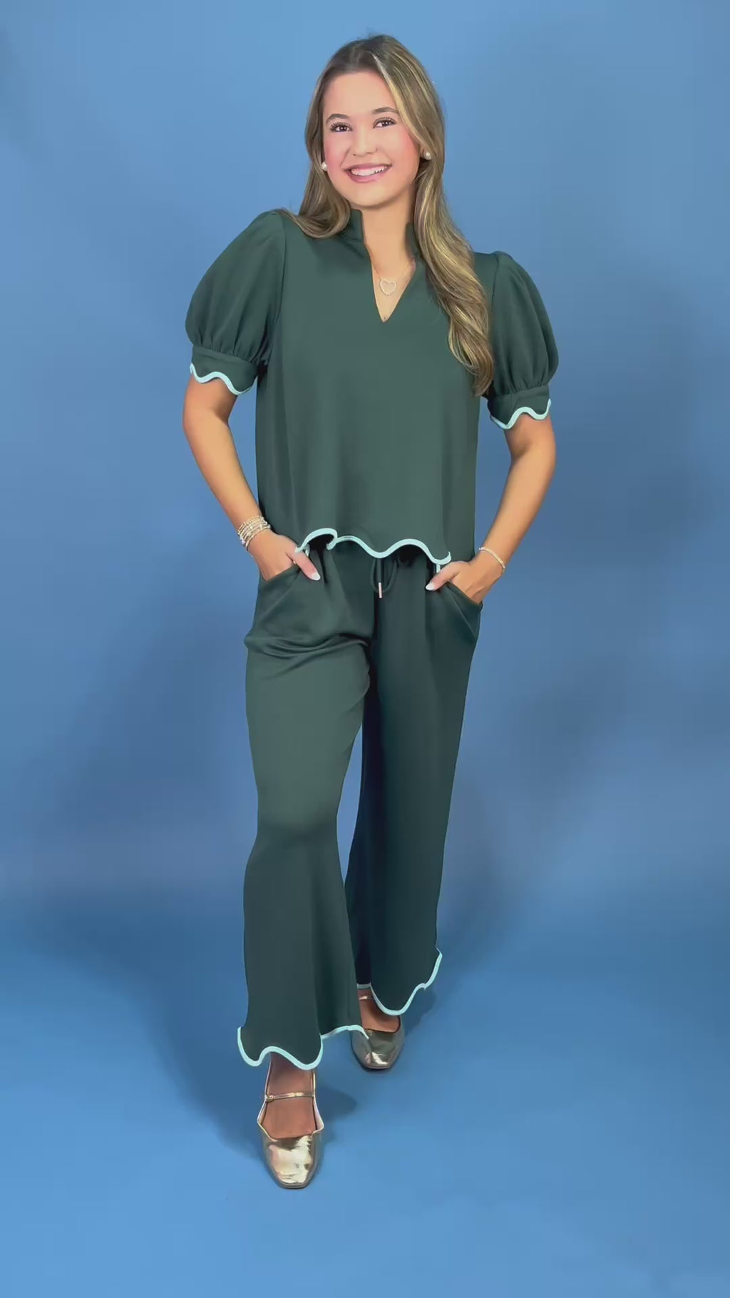 a dark green two-piece outfit consisting of a short-sleeve top with puff sleeves and a scalloped hem, paired with matching wide-leg pants with white piping trim