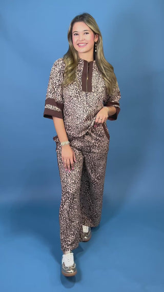 A woman modeling a matching two-piece leopard print lounge set with brown trim