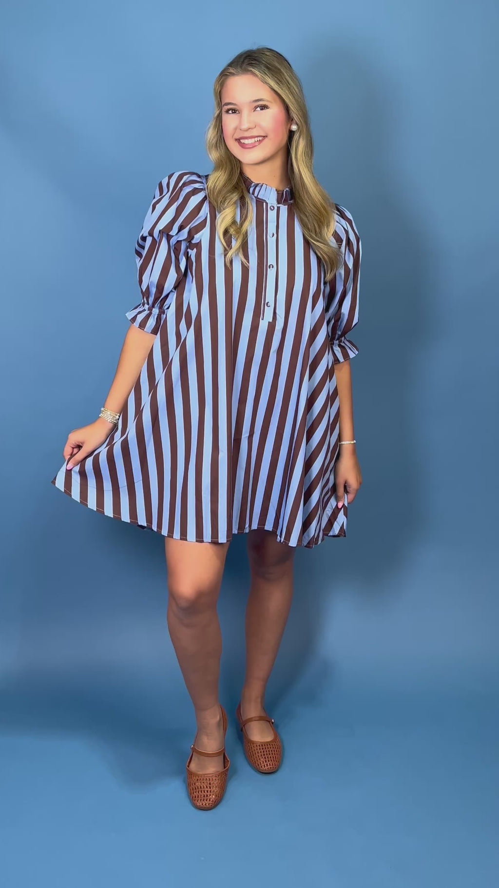 A woman modeling a brown and light blue vertically striped mini dress with puff sleeves and a buttoned collar