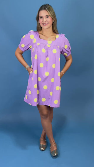 A young woman modeling a lavender purple short-sleeve dress with large yellow polka dots