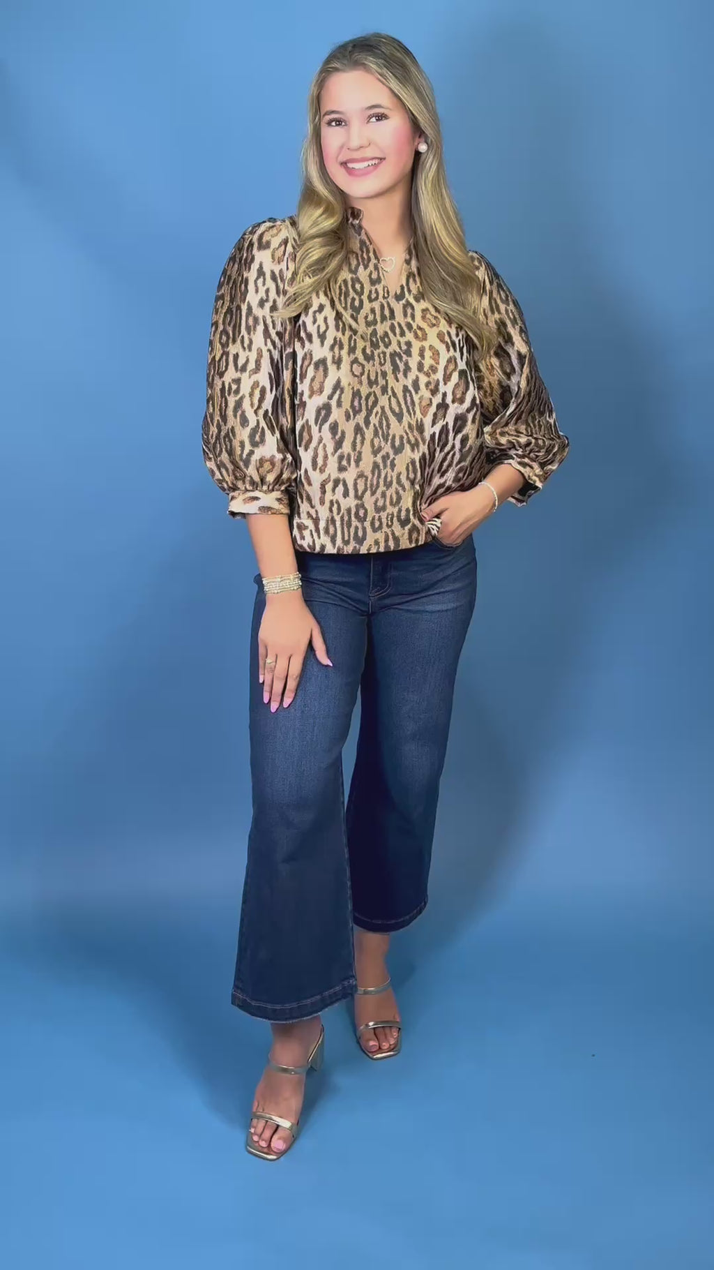 A woman wearing a leopard print long-sleeve blouse with puffed sleeves and dark blue jeans