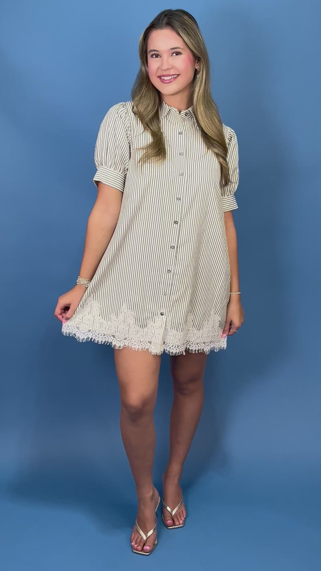 A woman modeling a short-sleeve button-front shirt dress with thin vertical stripes, puff sleeves, and lace trim at the hem