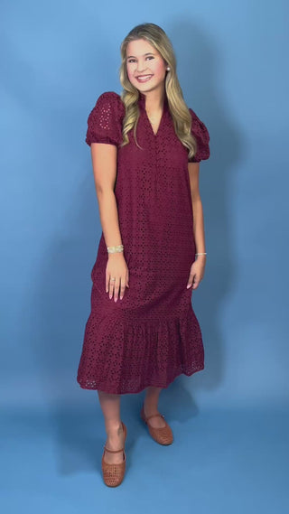 A woman modeling a short-sleeve burgundy eyelet lace midi dress with puff sleeves