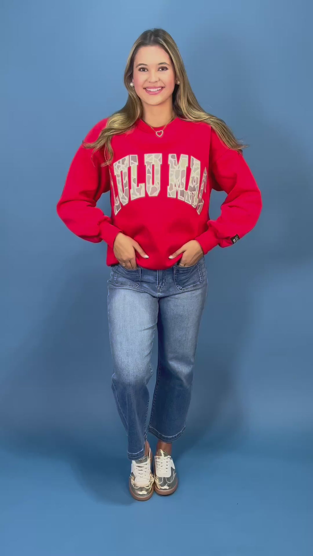 A woman modeling a bright red crewneck sweatshirt with 'LULU MAC' printed in white varsity-style letters