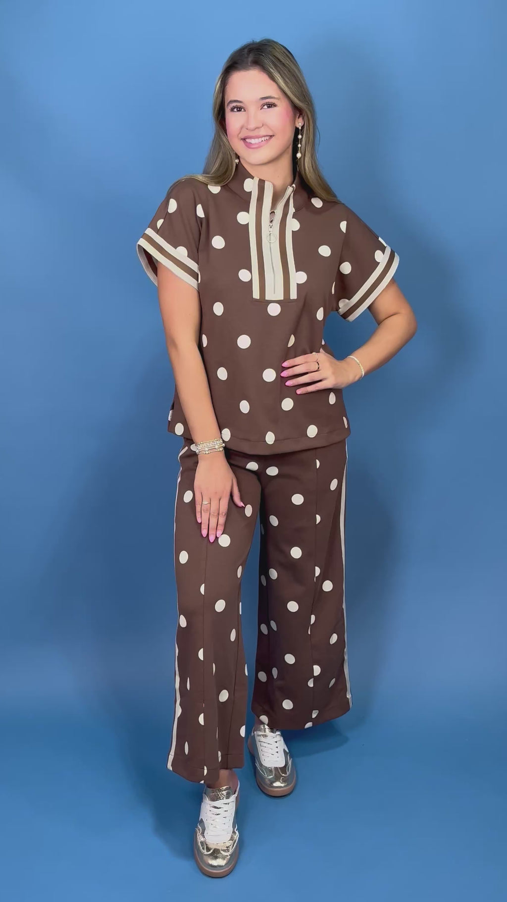 A woman modeling a brown two-piece lounge set with white polka dots, featuring a short-sleeve top with cream trim and matching wide-leg pants
