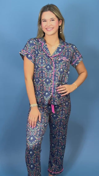 A woman modeling a matching two-piece pajama set with a navy blue floral print, pink piping, and a pink drawstring