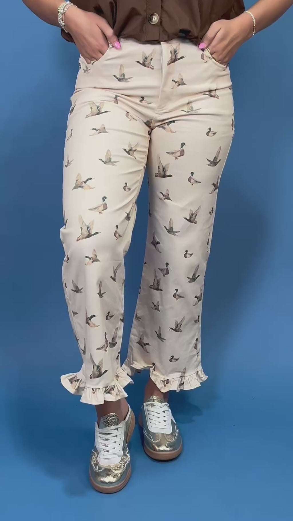 A person wearing cream-colored cropped pants with a brown and gray duck print, paired with a brown top and metallic silver sneakers