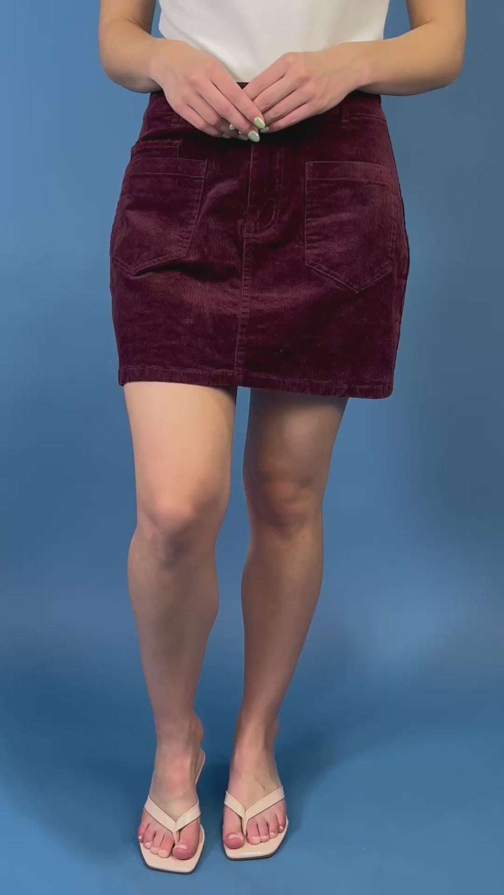 Burgundy corduroy mini skirt featuring a high-rise fit, front patch pockets, button-and-zip closure, and a structured straight silhouette.