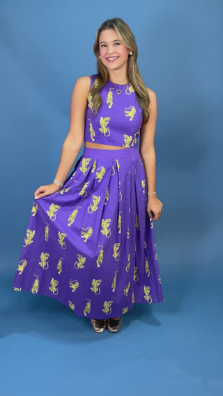A woman modeling a purple sleeveless dress with yellow tiger prints against a solid blue background.