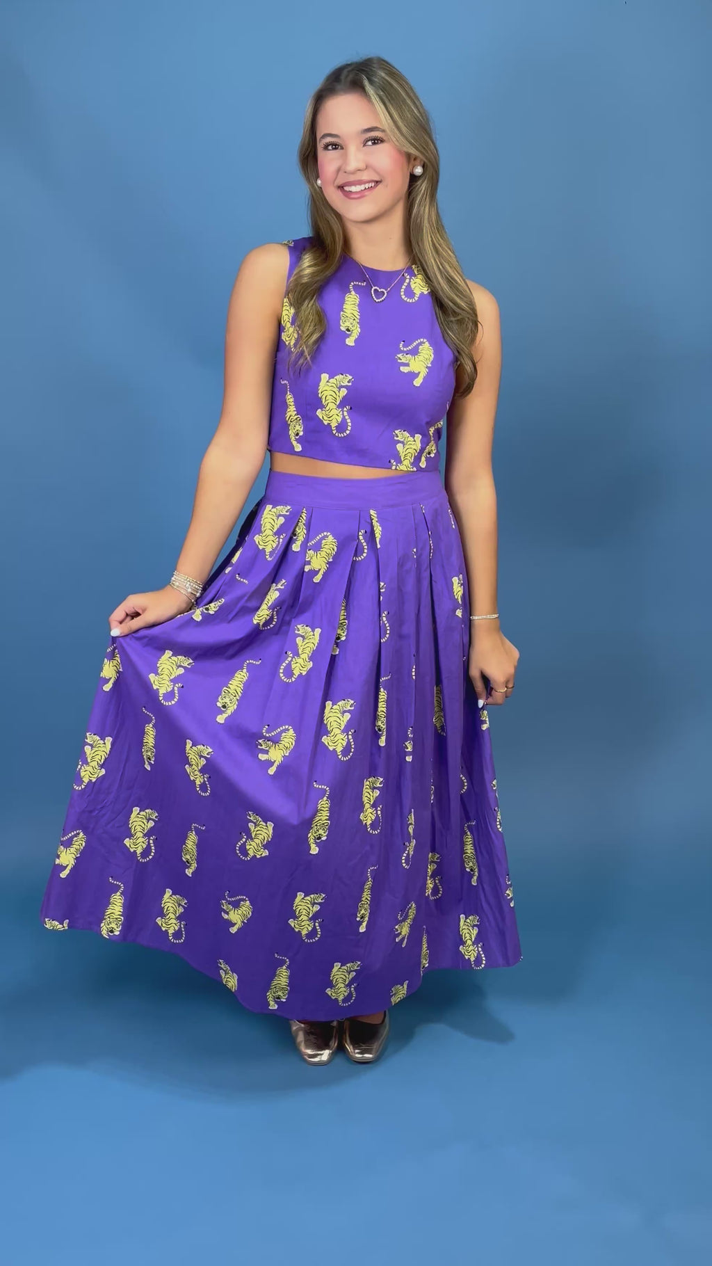 A woman modeling a purple sleeveless dress with yellow tiger prints against a solid blue background.