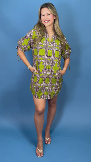 A woman modeling a short-sleeve mini dress with a green, white, and brown dragonfly pattern