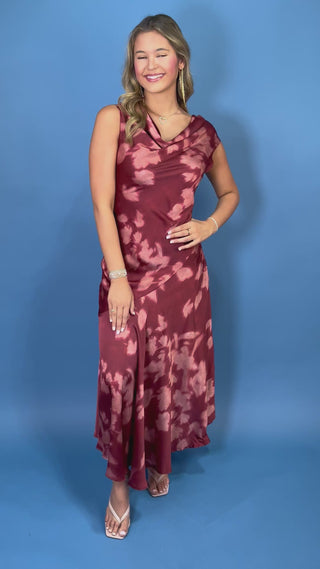 Burgundy floral satin maxi dress with a draped cowl neckline, sleeveless silhouette, and elegant flowing skirt.