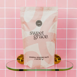 Bag of 'sweet grace' mineral soaking salts on a glass shelf against a pink tiled wall.