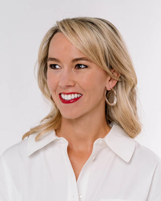 Woman with blonde hair and red lipstick wearing a white shirt on a light background