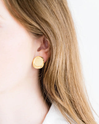 Gold earring worn by a person with blonde hair on a white background