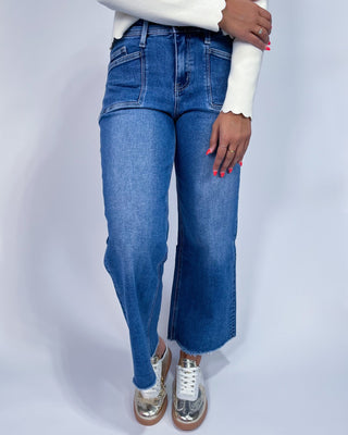 A person wearing medium-wash blue denim jeans with a straight-to-wide leg fit,