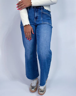A person wearing medium-wash blue denim jeans with a straight-to-wide leg fit,