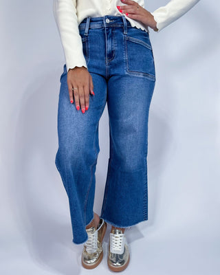 A person wearing medium-wash blue denim jeans with a straight-to-wide leg fit,