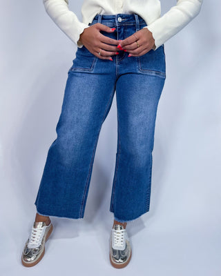 A person wearing medium-wash blue denim jeans with a straight-to-wide leg fit,