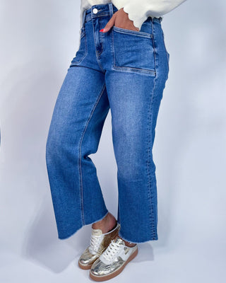 A person wearing medium-wash blue denim jeans with a straight-to-wide leg fit,