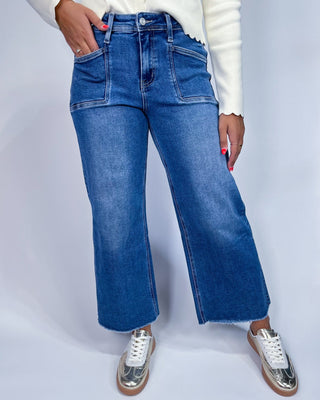 A person wearing medium-wash blue denim jeans with a straight-to-wide leg fit,