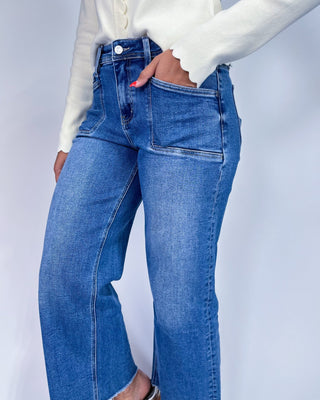 A person wearing medium-wash blue denim jeans with a straight-to-wide leg fit,