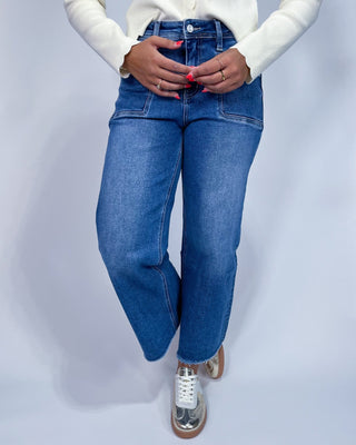 A person wearing medium-wash blue denim jeans with a straight-to-wide leg fit,