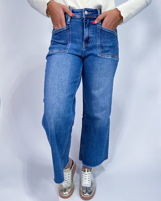 A person wearing medium-wash blue denim jeans with a straight-to-wide leg fit,