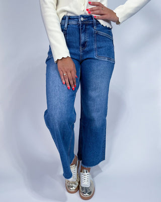 A person wearing medium-wash blue denim jeans with a straight-to-wide leg fit,