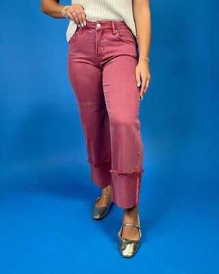 A person wearing dusty rose wide-leg jeans with frayed rolled hems, paired with a cream ribbed top and metallic flats