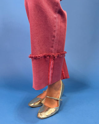 A person wearing dusty rose wide-leg jeans with frayed rolled hems, paired with a cream ribbed top and metallic flats