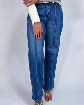 A person wearing medium-wash blue straight-leg jeans with contrast light stitching, styled with a white long-sleeve top and m