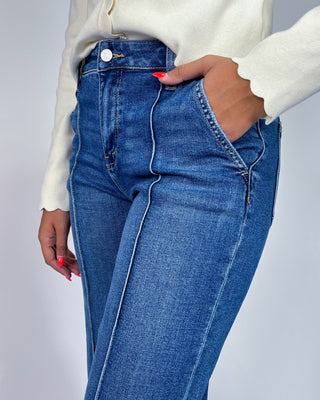 A close-up of a person wearing high-waisted blue denim jeans with contrast light stitching, paired with a cream-colo
