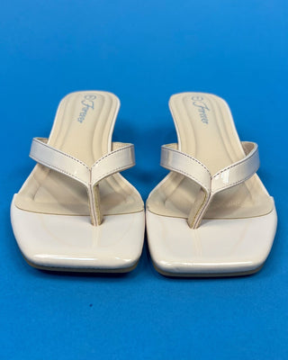 A pair of glossy off-white patent leather thong sandals with square toes and low block heels, displayed against a solid b
