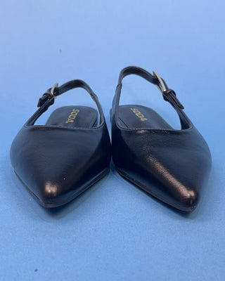 A pair of black leather pointed-toe slingback flats with gold 'SODA' branding on the insoles, set against a solid blue b8