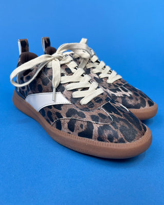 A pair of low-top sneakers featuring a brown and black leopard print pattern, a white side stripe, cream-colored laces,