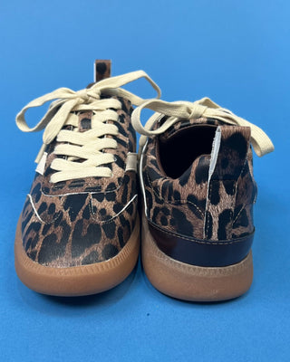A pair of low-top sneakers with a brown and black leopard print pattern, cream-colored laces, and tan soles, shown from th