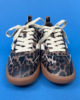 A pair of low-top sneakers with a brown and black leopard print pattern, cream-colored laces, and gum soles, photographed