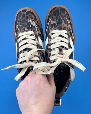 A pair of low-top sneakers with a brown and black leopard print pattern, cream-colored laces, and white side stripes,