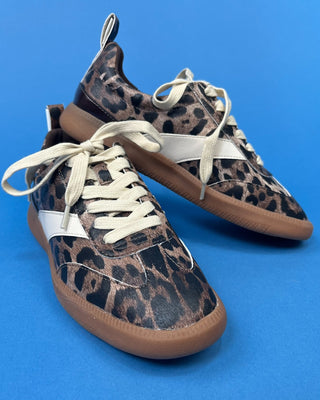 A pair of low-top sneakers with a brown and black leopard print pattern, featuring off-white laces and a white side stripe