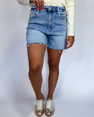 A person wearing light blue denim cut-off shorts with frayed hems