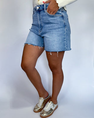 A person wearing light blue denim cut-off shorts with frayed hems