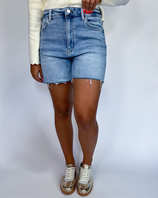 A person wearing light blue denim cut-off shorts with frayed hems