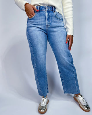 A person wearing light blue high-waisted straight-leg jeans, a white long-sleeve top, and metallic silver sneakers, shown fr