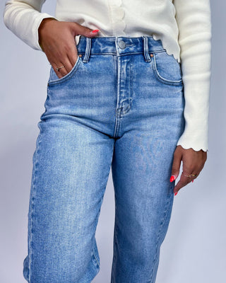 A close-up of a person wearing light blue high-waisted denim jeans with a cream-colored long-sleeve top, showing the fi