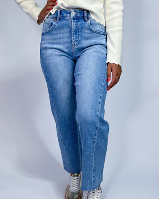 A person wearing light blue high-waisted straight-leg jeans, a white long-sleeve top, and white sneakers, shown from the